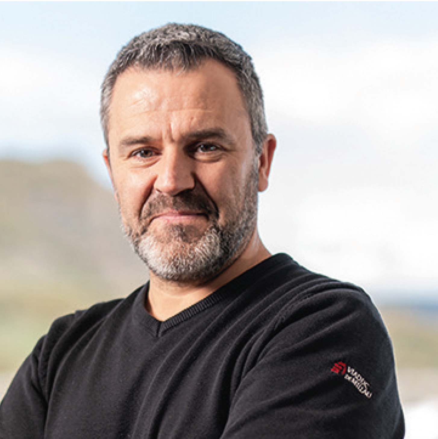 Portrait d’Éric Laporte. Il porte un pull noir, a le teint hâlé, des cheveux et une barbe poivre et sel.