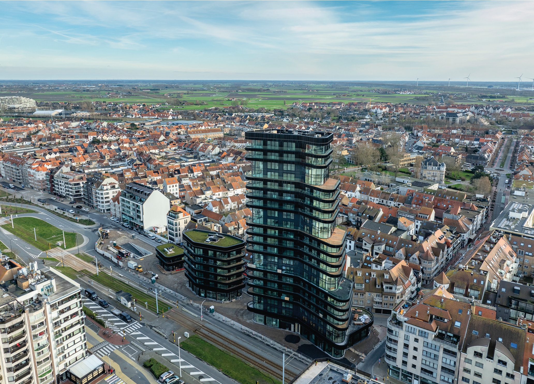 Aerial view of a black tower with lots of windows standing out against a landscape of tiled-roofed houses.